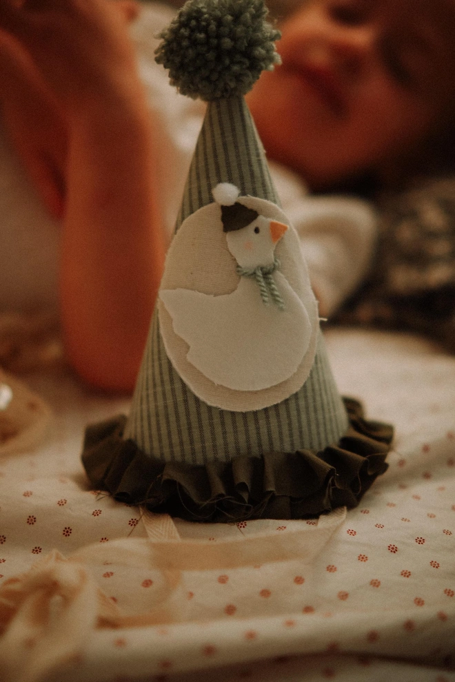 Baby Birthday Hat With Goose, a child lying with their birthday hat with a goose on a bed. 