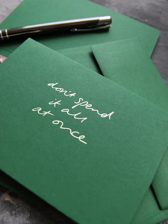 Hand foiled cash card or money wallet in a forest green colour handfoiled in shiny lime green text which says 'don;t spend it all at once' which has a matching forest green envelope