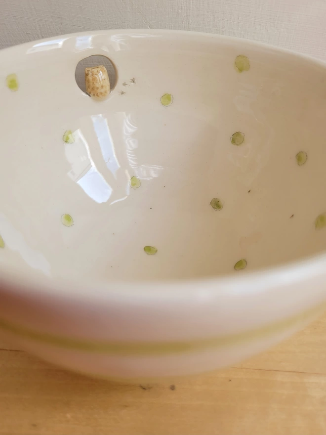 close up shot of the inside of a ceramic bowl with green dots inside an off white bowl showing a cut out near the top of the dish with a pale brown owl with bird prints 