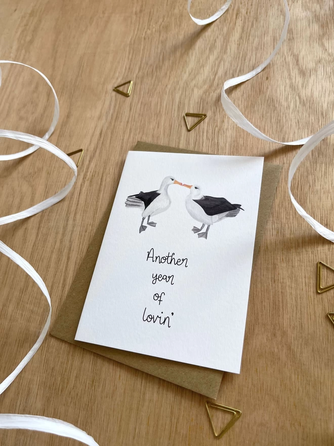 a greetings card featuring two albatross birds kissing with the wording “another year of lovin’”