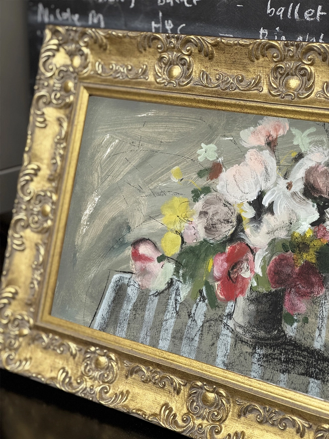 a print of a painterly floral bouquet with a sketchy feel and stripy tablecloth in an ornate gold frame