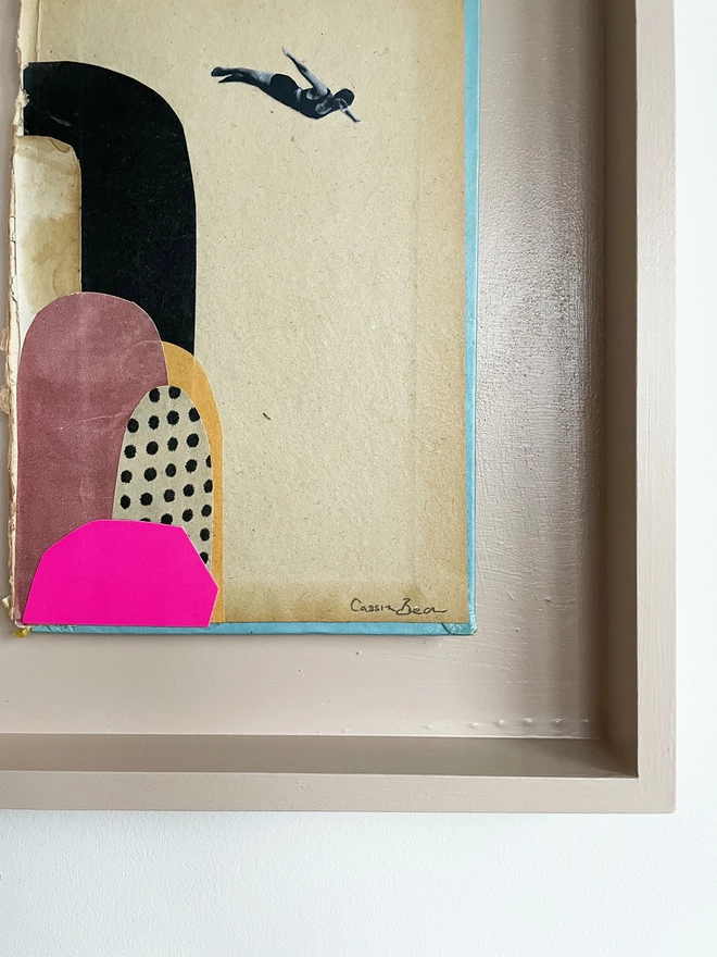 A diving portrait artwork on a vintage book cover, float mounted within a pale pink wood frame.