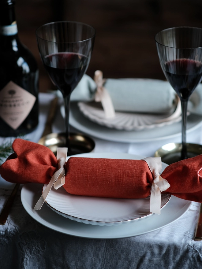Reversible reusable linen Christmas crackers in soft pink, sage green, cream and muted festive colours, tied with natural ribbon and arranged on a family Christmas table