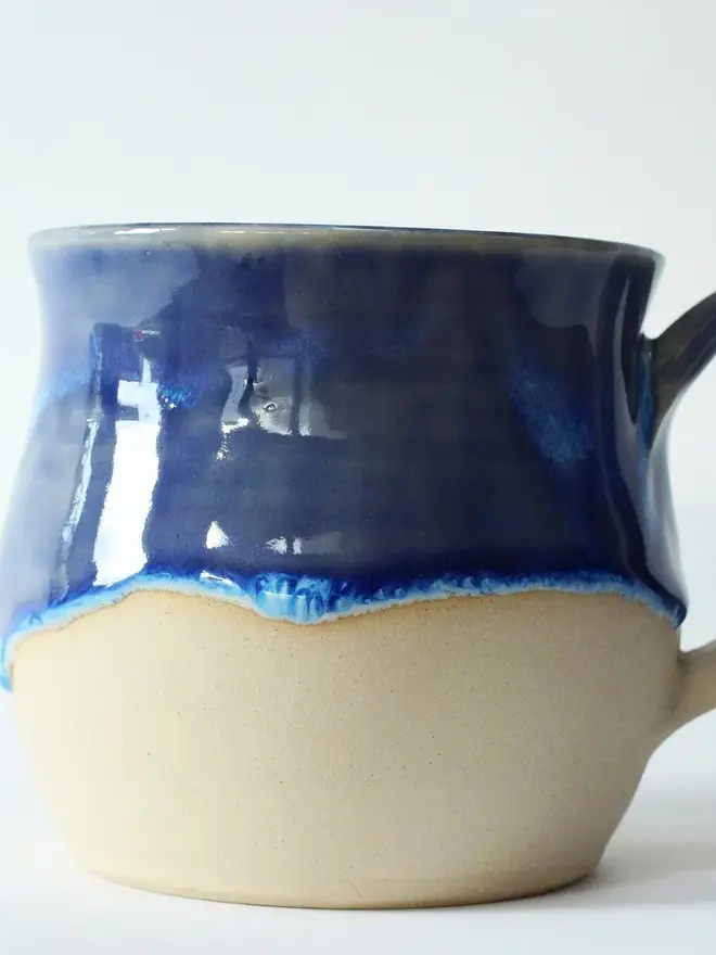 “Sea, please” ceramic mug with a glossy blue top glaze and natural ceramic bottom, placed against a plain white background.