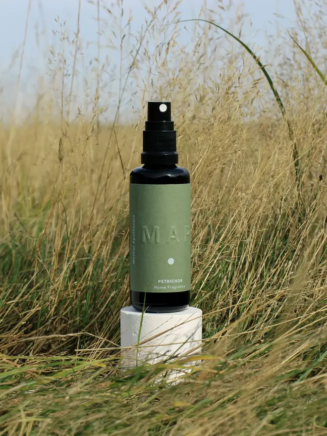 petrichor earthy home fragrance spray. spray bottle photographed in grassy field.