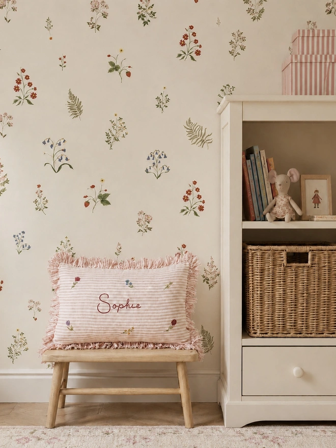 Personalised pink striped stonewashed linen cushion with ruffle trim, hand-painted ditsy florals and embroidered name, styled in a floral children’s bedroom.
