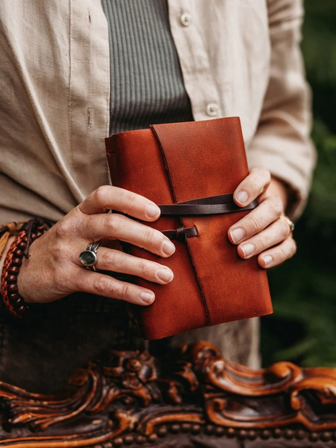 make your own leather journal. a red-brown leather journal held in hands.