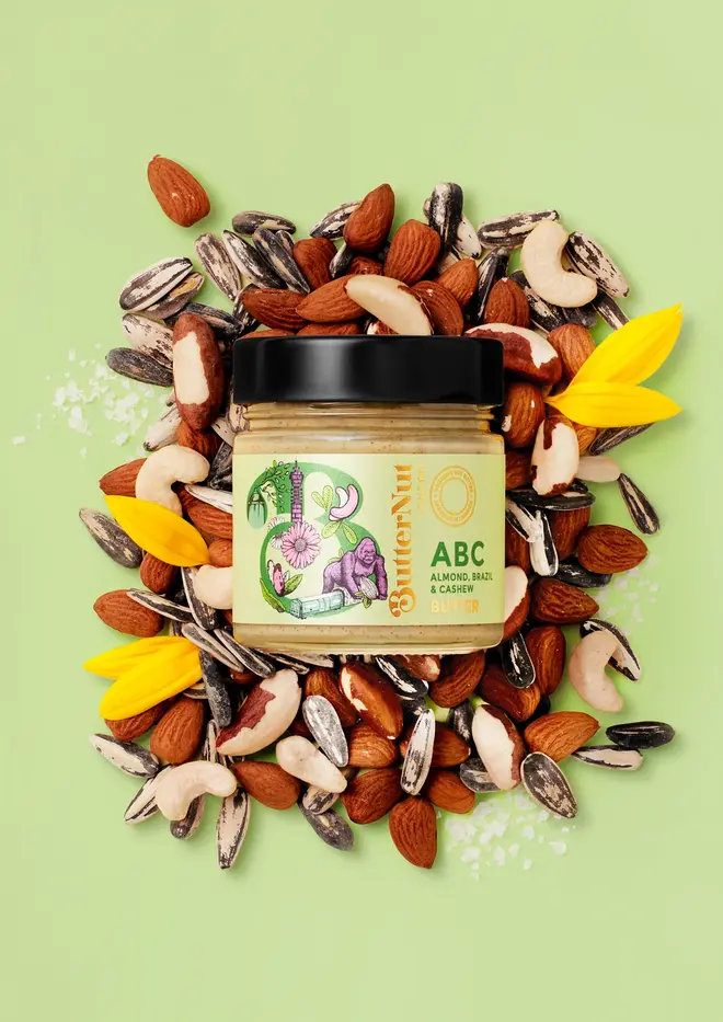 almond, brazil nut and cashew butter. a jar of nut butter photographed against a light green background, surrounded by assorted nuts.