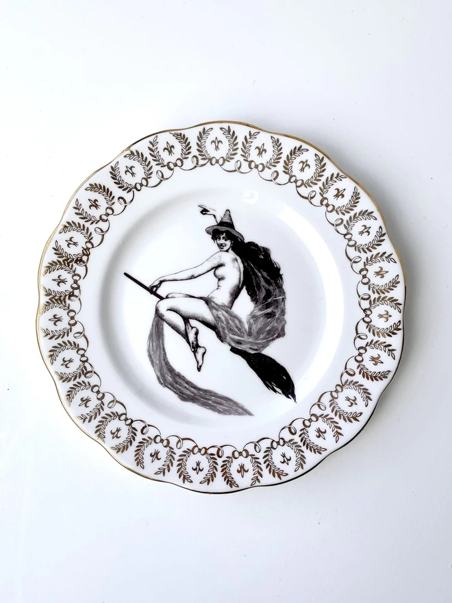 vintage plate with an ornate border, with a printed vintage illustration of a witch on a broomstick in the middle 
