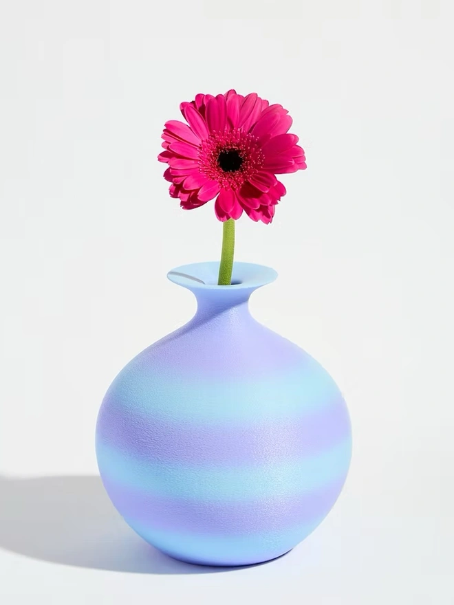 3d printed vase in blue and purple stripes with bright pink flower