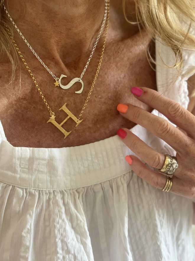 model wears sterling silver S letter charm on silver chain with gold mini star charm and gold plate H letter charm on gold chain with gold mini star