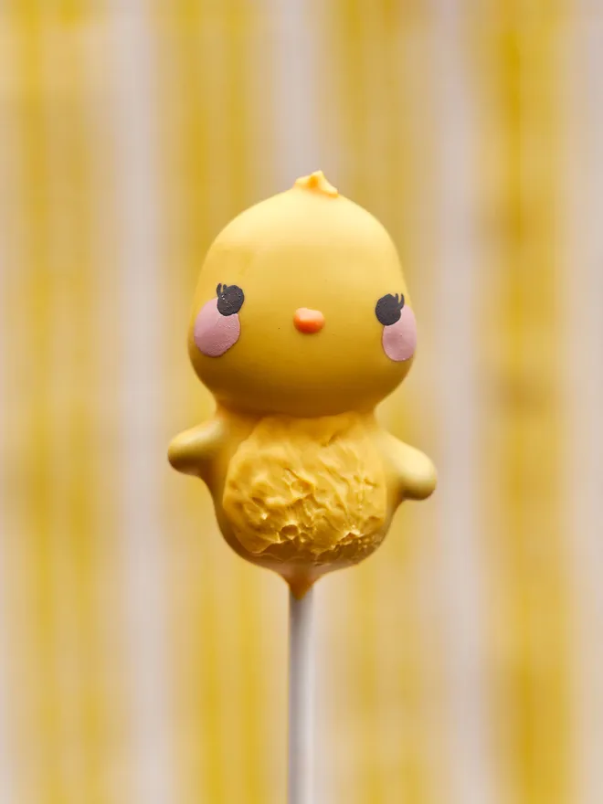 Easter chick cake pop, placed infront of a yellow and white stripy background 