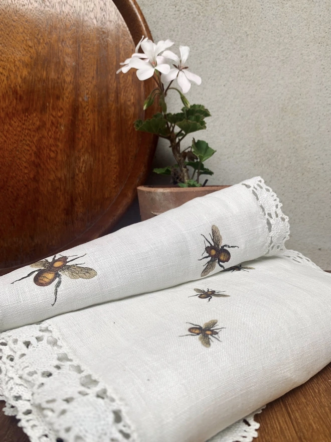 A linen and lace table runner with printed bees in front of a mid century wooden tray