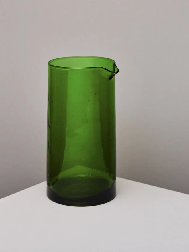 Glass Carafe, a large green glass jug sitting on a plain counter top against a grey backdrop. 