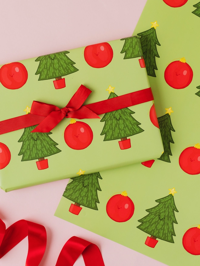 Green Christmas wrapping paper featuring a repeating pattern of hand-drawn Christmas trees with yellow stars and red Christmas baubles.