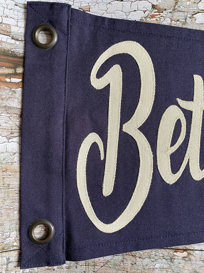 Detail of a navy 'Better Together' pennant flag. This shows the letters BET written in ivory canvas.