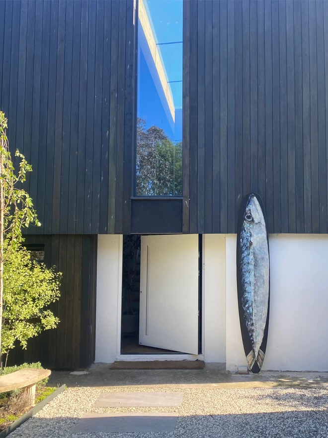 big mackerel painted surfboard displayed outside a contemporary house