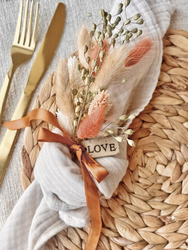 knotted napkin holding a pink flower posy, tied with a ceramic tag with the word 'love'