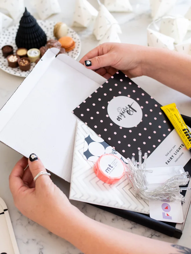 Woman's hands holding origami kit open with instructions, glue, papers and washi tape inside