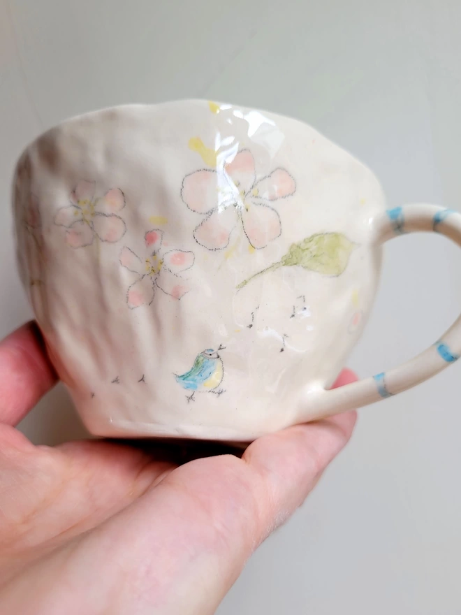 hand made pottery tea cup with pink flowers and a bluetit walking leaving bird prints and musical notes on the mug