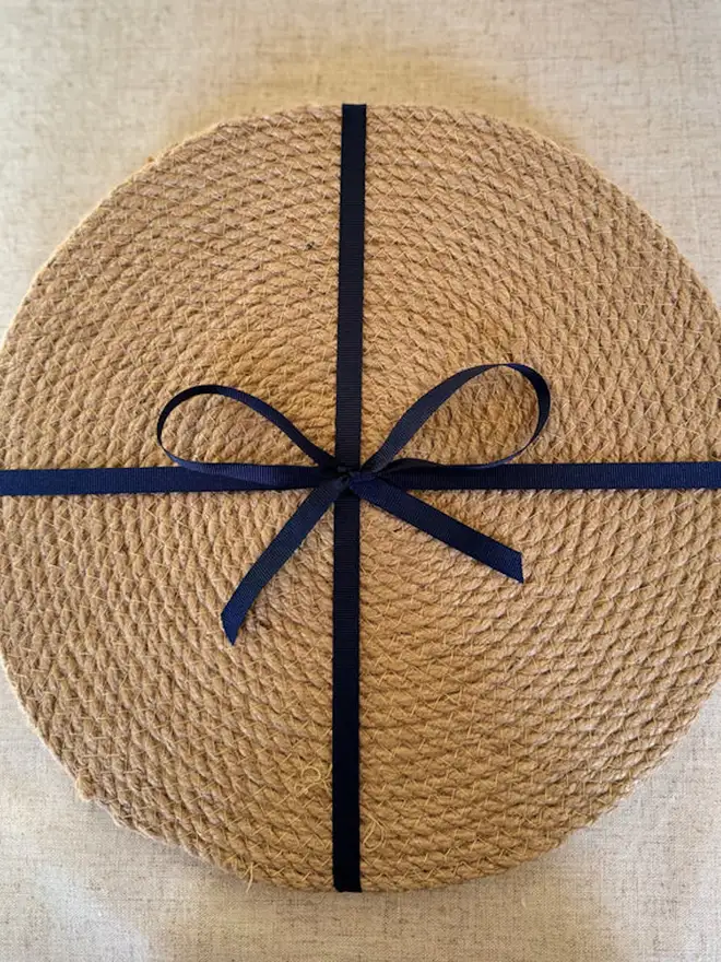 Close up of a round woven seagrass neutral placemats shown on a light surface with a black bow around them. 