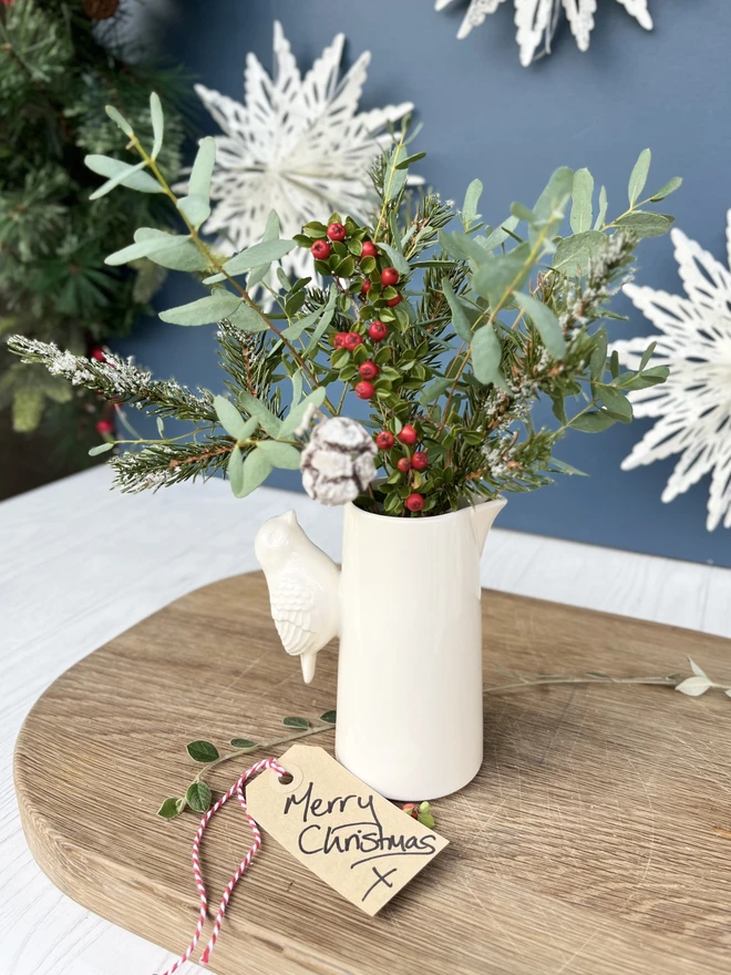 Jug with a detailed bird handles holding Christmas foliage 