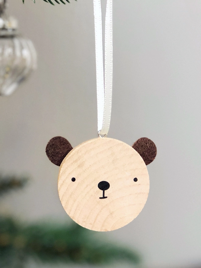 A small wooden and felt bear decoration hangs on a Christmas tree branch.