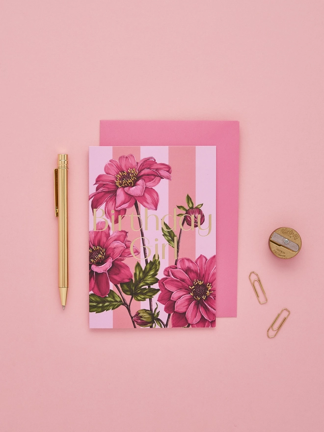 'Birthday Girl' card with gold foil wording and illustrated Dahlia flower on a pink and lilac striped base and a hot pink envelope