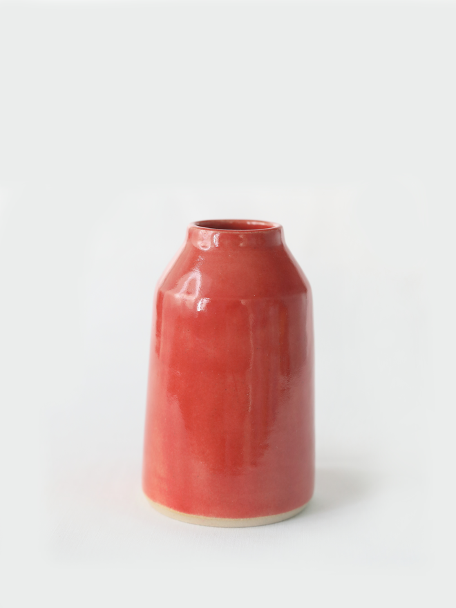 A small handmade ceramic bud vase in glossy cherry red glaze, with a rounded bottle shape and narrow neck, photographed against a plain white background