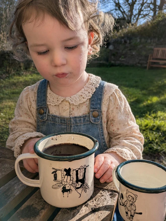 cute child playing with an enamel vintage style mug featuring pixie friends