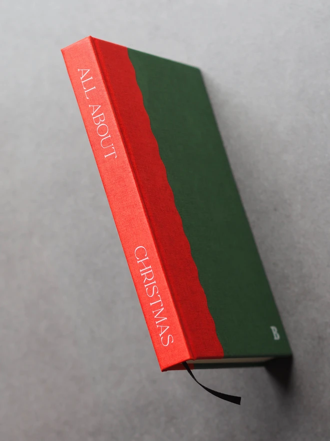 A two tone hardcover book in red and green, with "all about Christmas" printed down the spine in white ink, and an initial B stamped on the front cover in white ink