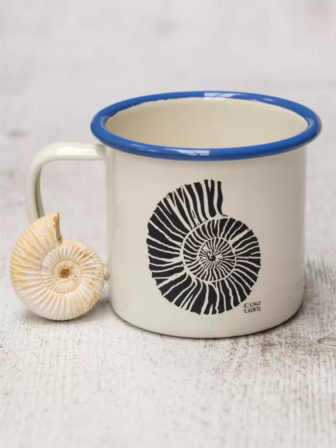 Picture of a Cream Enamel Mug with a Blue Rim with a Ammonite design etched onto it, taken from an original Lino Print