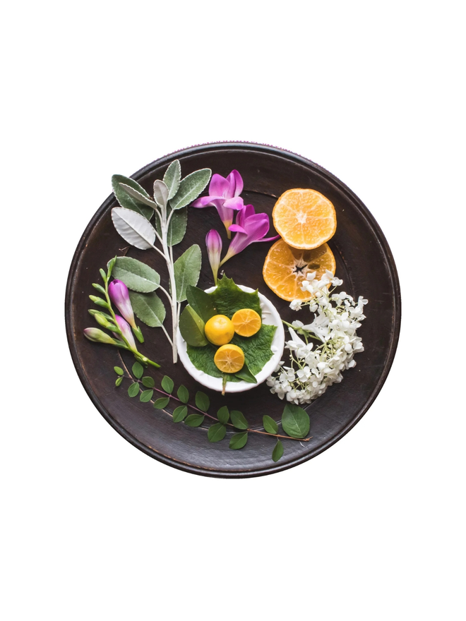 frangipani and orange blossom botanical hand cream. a round tray holding natural ingredients.