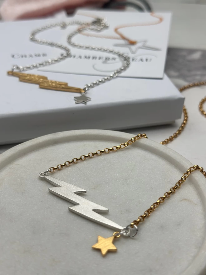 sterling silver chain with personalised gold electric bolt charm and a small silver star, and a gold chain with silver electric bolt and small gold star