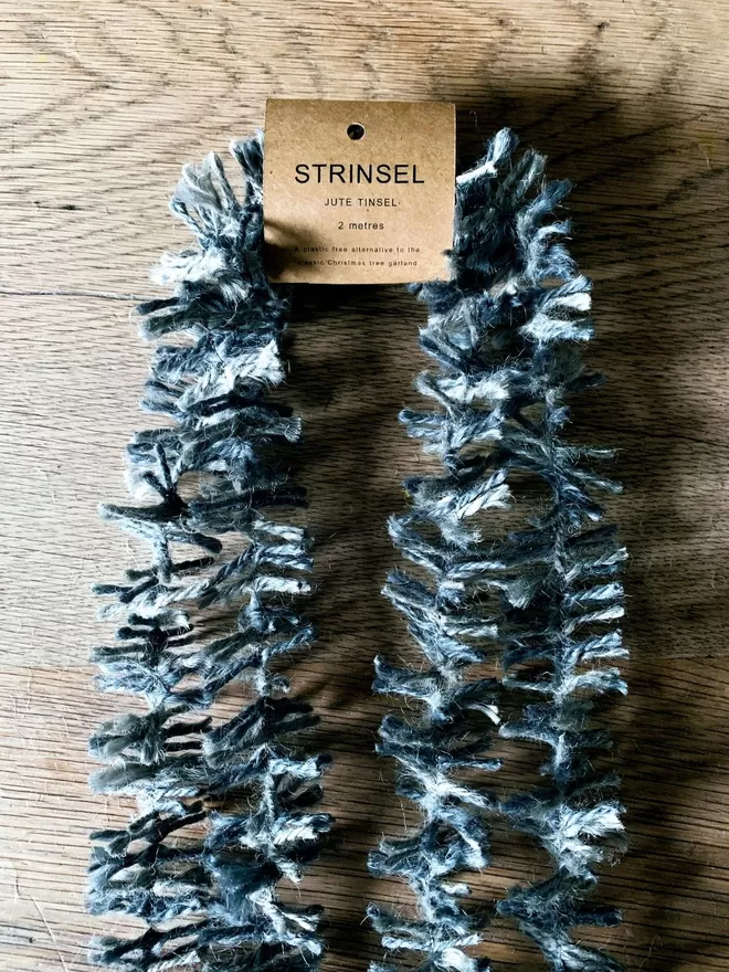 2 metre length of silver dyed jute Strinsel (plastic free string tinsel) with label on oak table