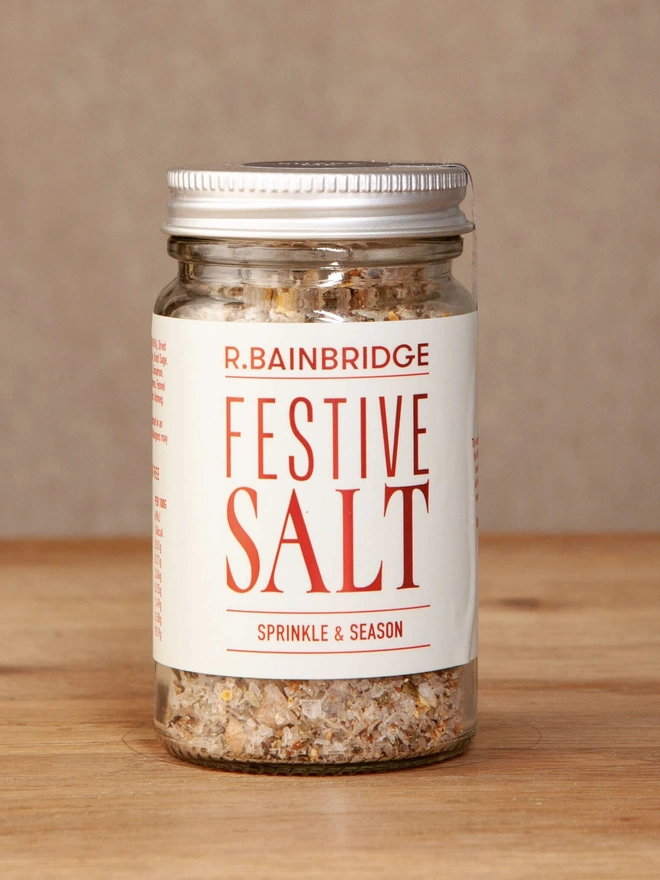 Festive Salt, a jar of salt sitting on a wooden surface against a plain backdrop. 