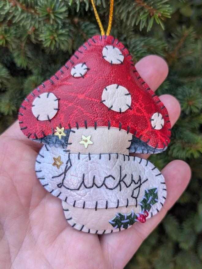 Hand stitched personalised toadstool Christmas decoration made from vegan-friendly faux leather, featuring a red mushroom cap, holly details and a personalised name banner.