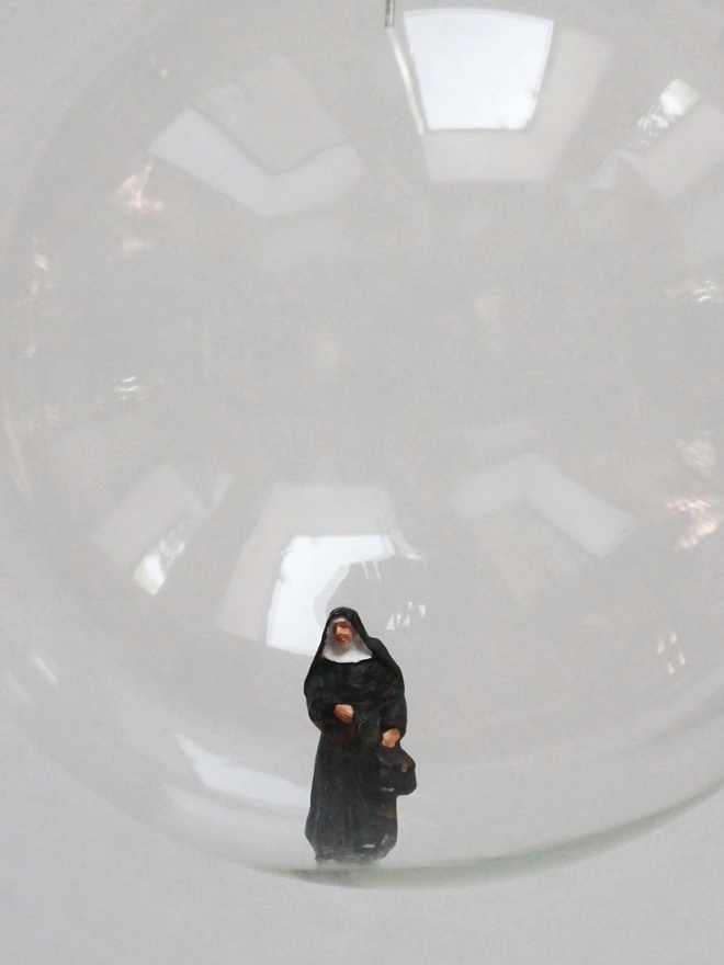 Miniature figure of a nun in a glass Christmas bauble - close up 