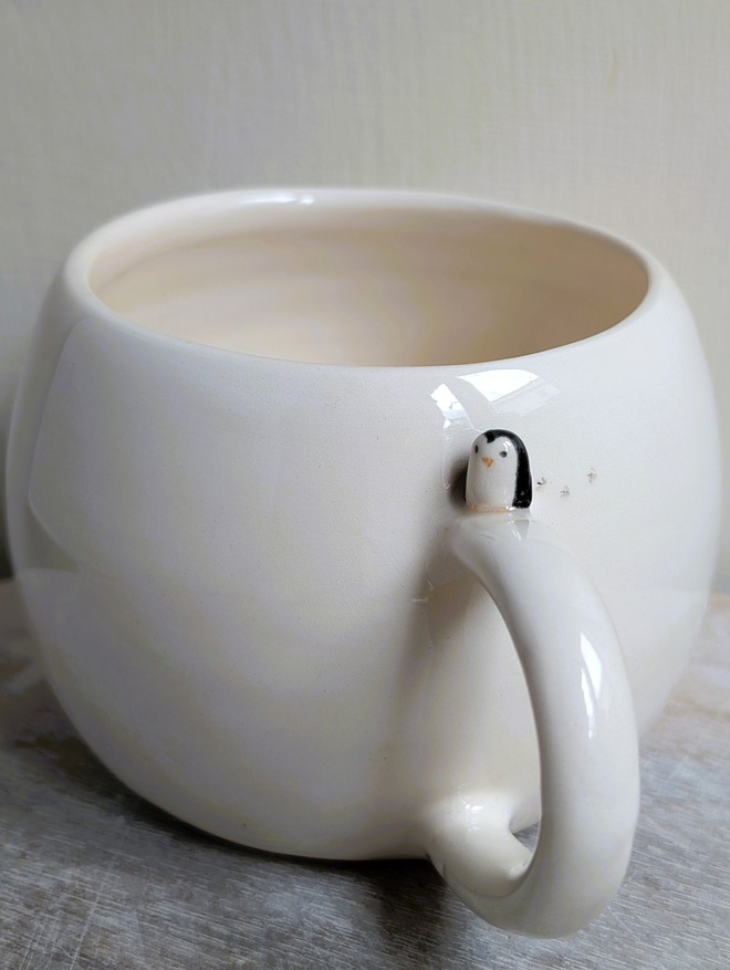 white cup with a tiny ceramic penguin on the handle 