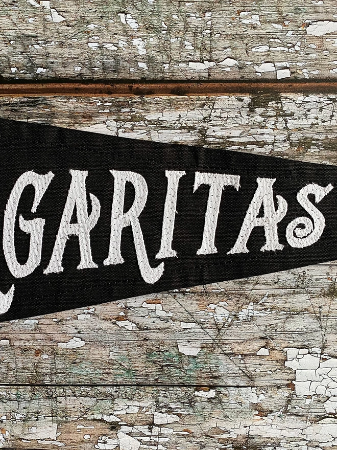 A close up of a section of Midnight margarita black pennant flag showing the letters in white GARITAS. 