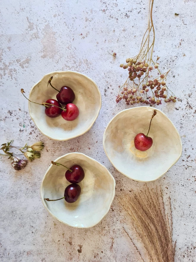 Triple mini ceramic bowls, pottery bowls, gifts, homeware, tableware, dip bowl, snack bowl, small bowl, Jenny Hopps Pottery, Dream Catcher, white cream, neutrals, photographed with dried flowers, cherries on a mottled white background