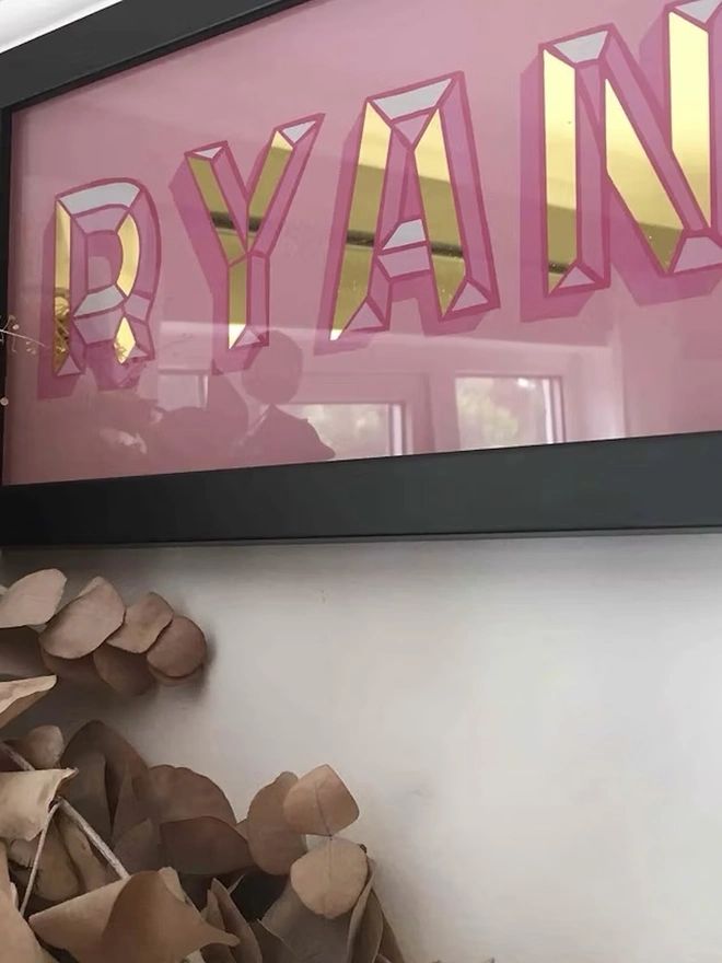 Personalised Name Wall Plaques, a pink personalised gold leaf sign sitting in a black frame hanging in front of a white wall. 