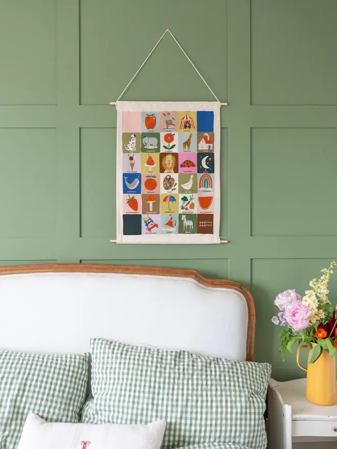 Colourful Rainbow Alphabet Fabric Banner, hanging on a green wall, next to a bed. 