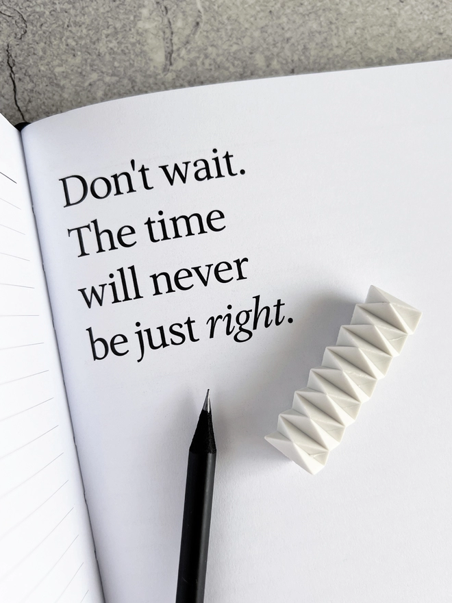 Quote page in the planner that reads "Don't wait. The time will never be just right." with a HELLO TIME pencil and White Zig Zag Eraser laid on top.