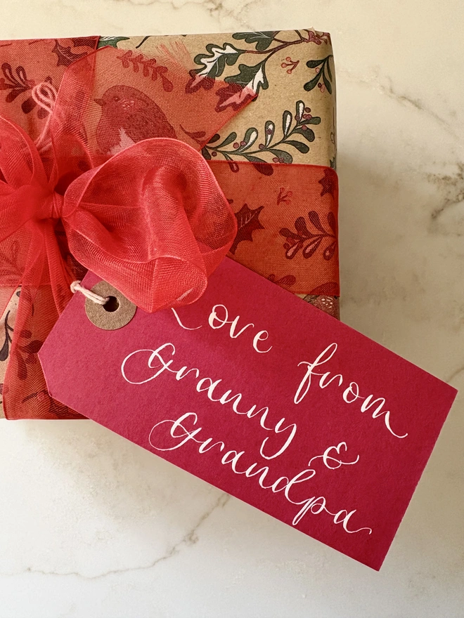 A large red luggage tag attached to  a Christmas present that reads Love from Granny & Grandpa