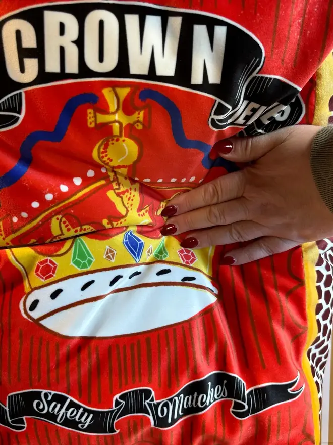 Crown Matchbox Cushion, a colourful red cushion sitting on a decorated surface. 