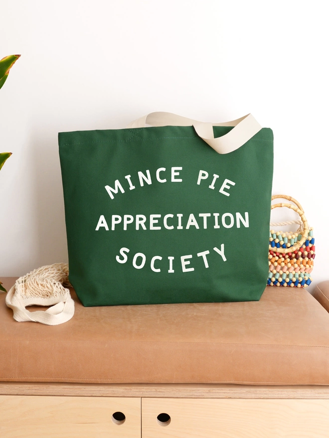 Green canvas Mince Pie Appreciation Society tote bag sitting on a bench