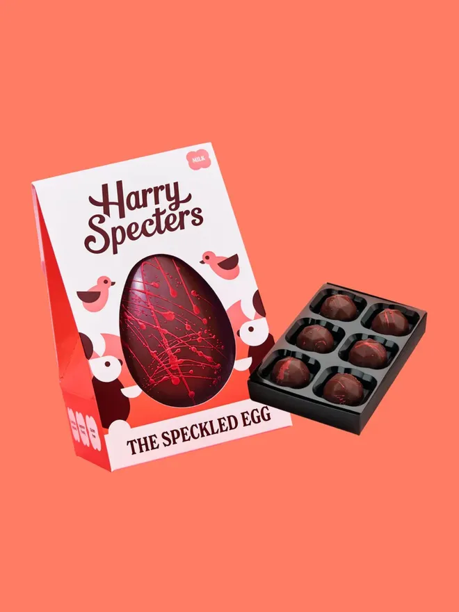 A milk chocolate Easter egg decorated with red speckles, next to a small box of luxury milk chocolates