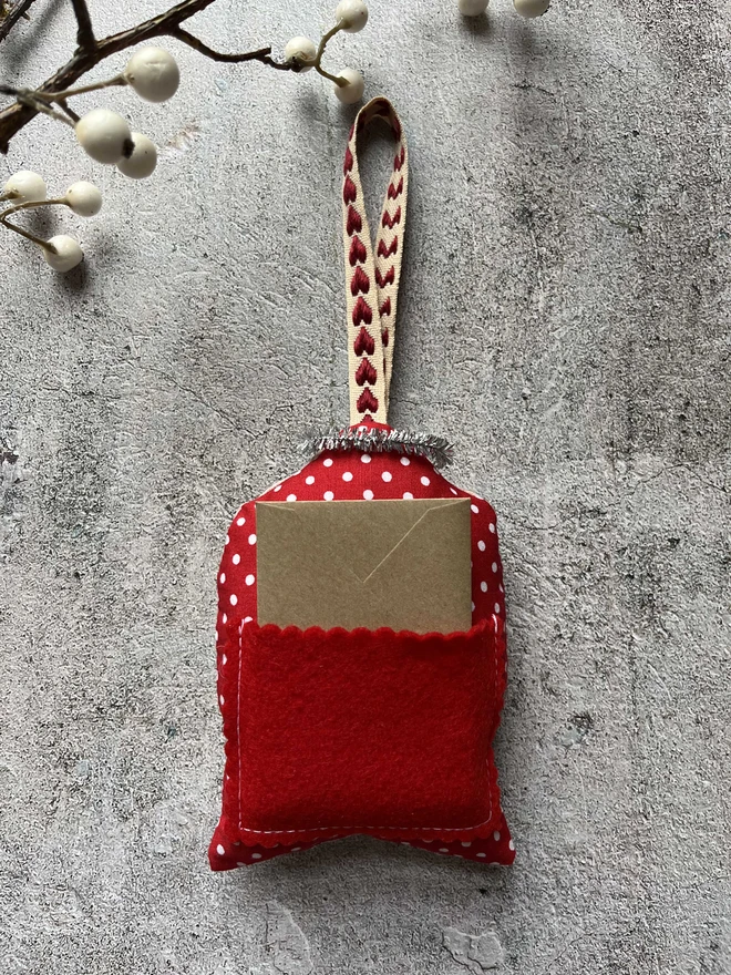 a photo of the back of the angel christmas tree decoration showing the red felt scalloped pocket holding the mini kraft envelope