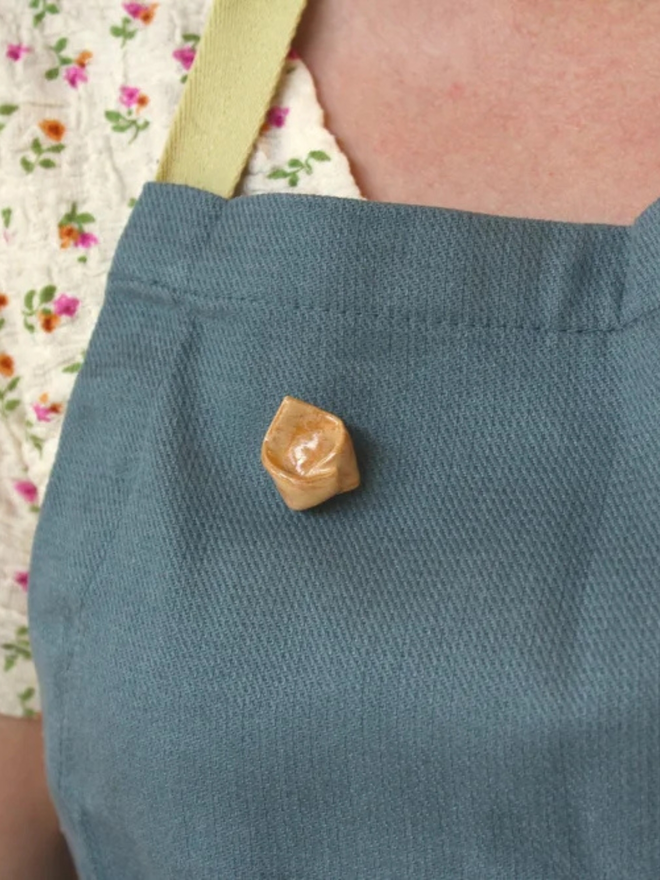 ceramic pasta pin badges. a ceramic tortellini badge photographed on an apron.